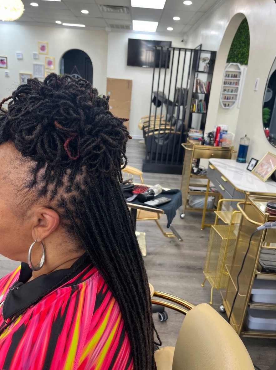 Woman with loc updo ponytail wearing pink yellow black top and hoop earrings — loc styling Delaware