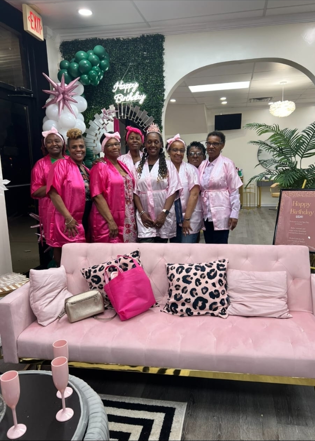 Group birthday spa party at Sinkor Beauty Salon Middletown DE — guests in pink robes, Happy Birthday neon sign, balloon décor